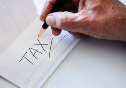 hand writing the word tax on a white paper